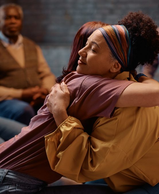 Supportive women embracing during group therapy at mental health center.