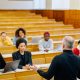 A diverse group of adult graduate students in a university classroom discussion with their instructor