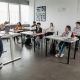 A teacher stands at the front of a bright classroom teaching a small group of diverse middle school students seated at desks